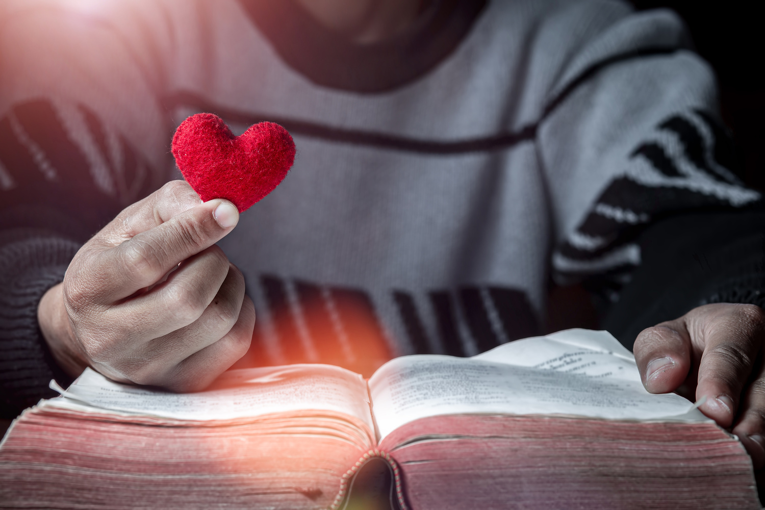 Holding Red heart in hand with Bible on wooden table, Close up, / surachat - stock.adobe.com Holding Red heart in hand with Bible on wooden table, Close up, love of christian concept.