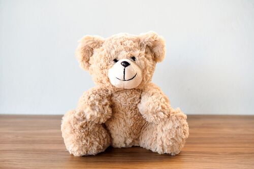 Cute Teddy Bear sitting alone with white cement wall on wooden table